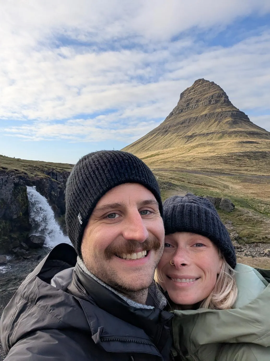 Sean and Ashley in Iceland, wind-blown, a mountain behind them.